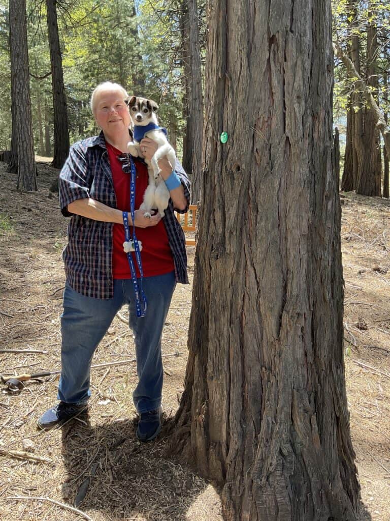 woman holding her dog in front of her memorial tree