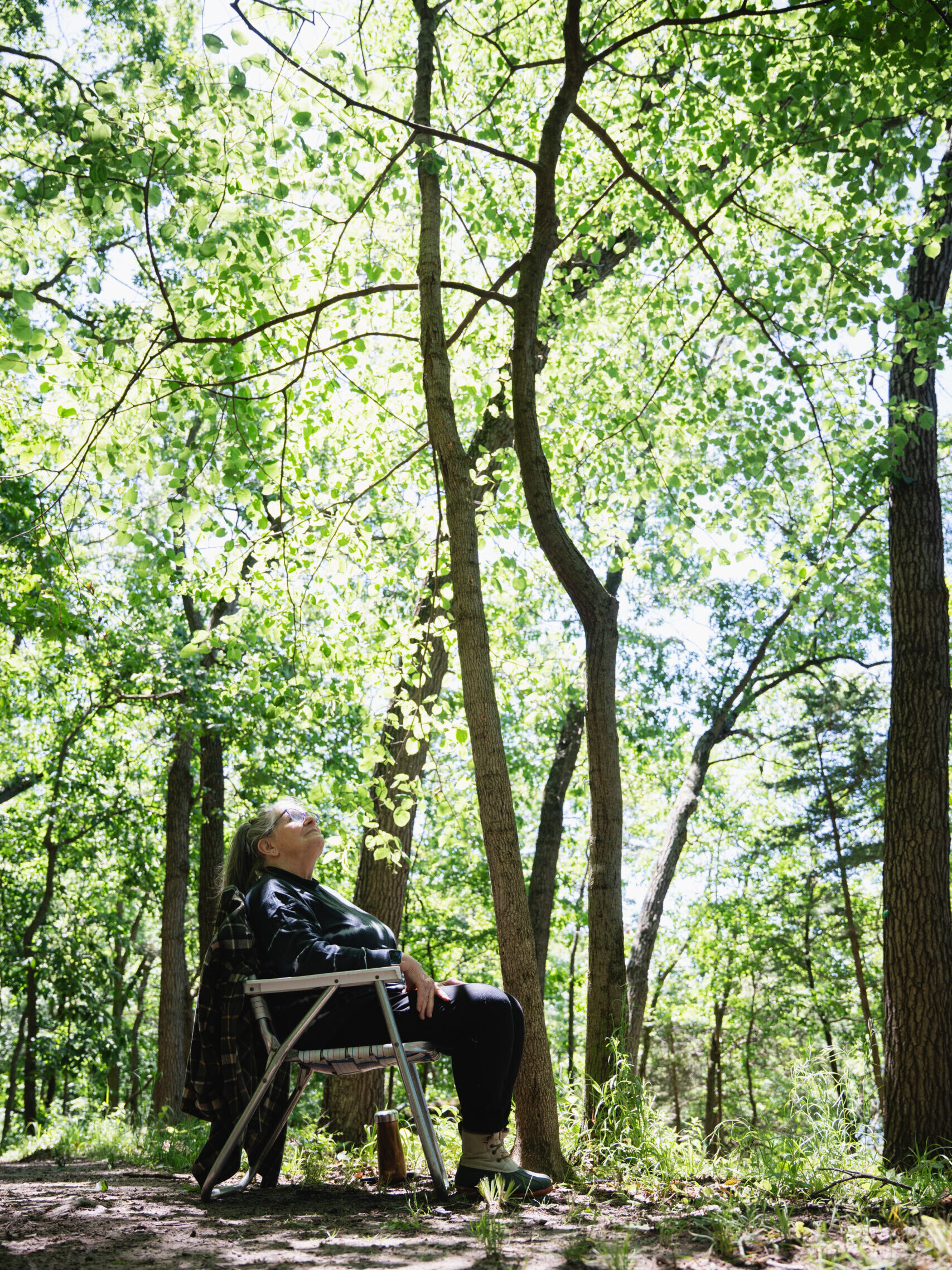 woman sits in her husbands folding chair and looks up at his memorial tree