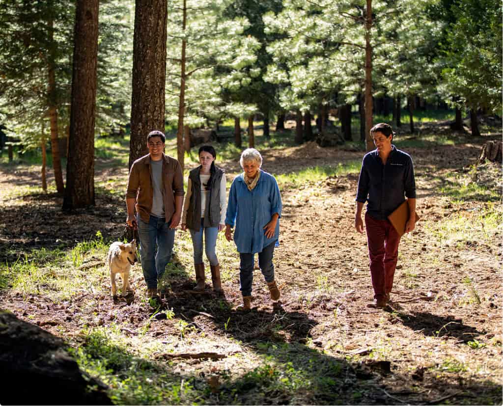 A family and a Guide walk together through a sunlit forest, with a dog on a leash.
